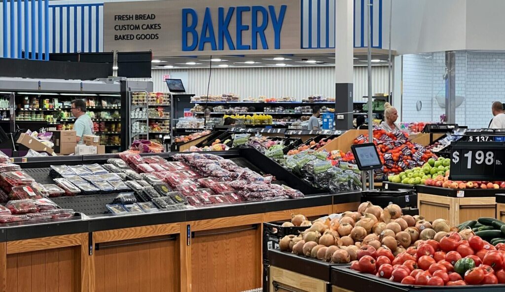 Modern grocery store produce section with fresh fruits and bakery signs.